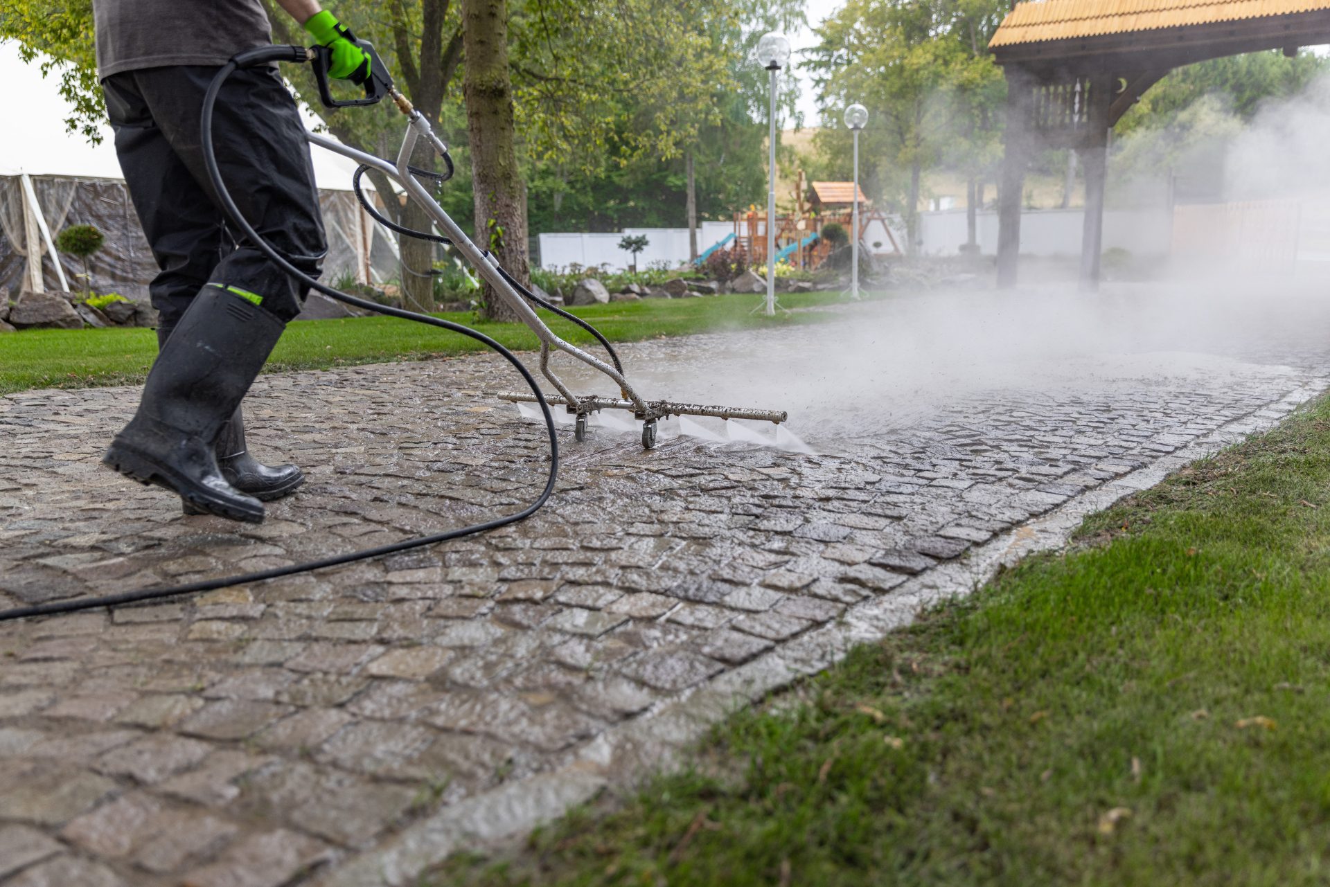Professional worker using a pressure washer surface cleaner on cobblestone